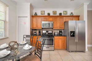 A kitchen with wooden cabinets, stainless steel appliances, a dining table with chairs, and a fire exit door.