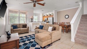 A spacious living room with a large sectional sofa, a ceiling fan, and a dining area with a table and chairs. - Resort Townhome w/ Pool Access & Outdoor Retreat (Kissimmee)
