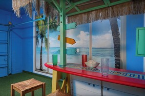 A room with a beach mural, a red bar counter, and a straw hat hanging from the ceiling.