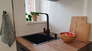Een keuken met een zwarte spoelbak, een houten aanrecht, een raam met een plant en een snijplank.
