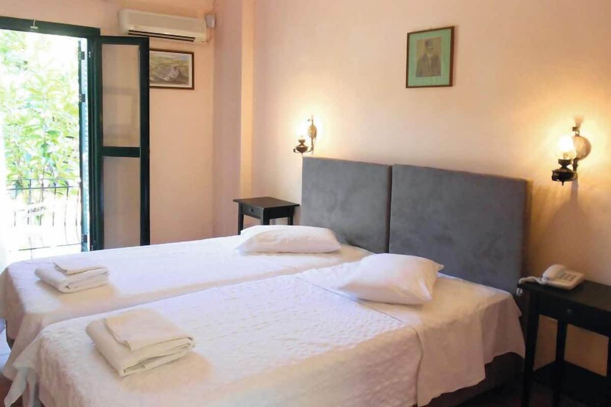A double bed with white linens, a bedside table with a lamp, and a wall-mounted phone.
