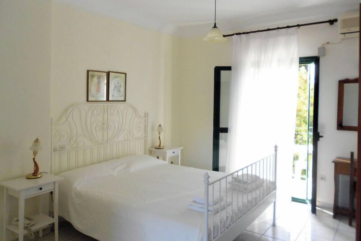 A bedroom with a white bed, bedside tables, a hanging lamp, and a door leading to a balcony.