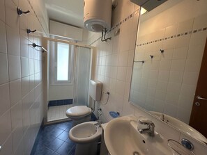 Un baño con inodoro, bidé, lavamanos y zona de ducha.