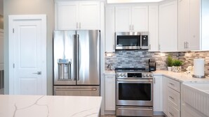 Una cocina moderna con armarios blancos, electrodomésticos de acero inoxidable, microondas, horno y encimera de mármol.