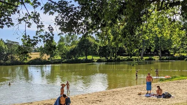 A lakeside setting with people relaxing on the sand, a boat, and a person walking by the water. - ZEcamping 3 étoiles piscine chauffée animaux acceptés mobil-home TV LV (Verruyes)