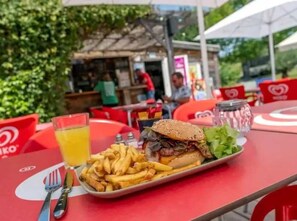 Un repas composé d’un hamburger et de frites, servi sur une table rouge avec une fourchette et un couteau.