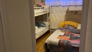 Ett sovrum med våningssängar, en byrå i trä och en färgglad täckfilt.