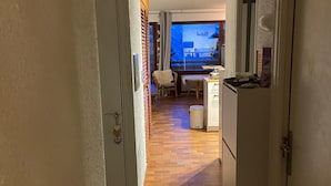 En smal hall med trägolv leder in till ett vardagsrum med en tv, ett matbord och en stol.