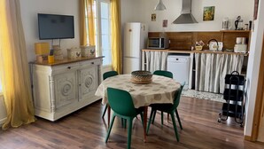 Een eetgedeelte met een ronde tafel, groene stoelen en een witte tafelkleed.