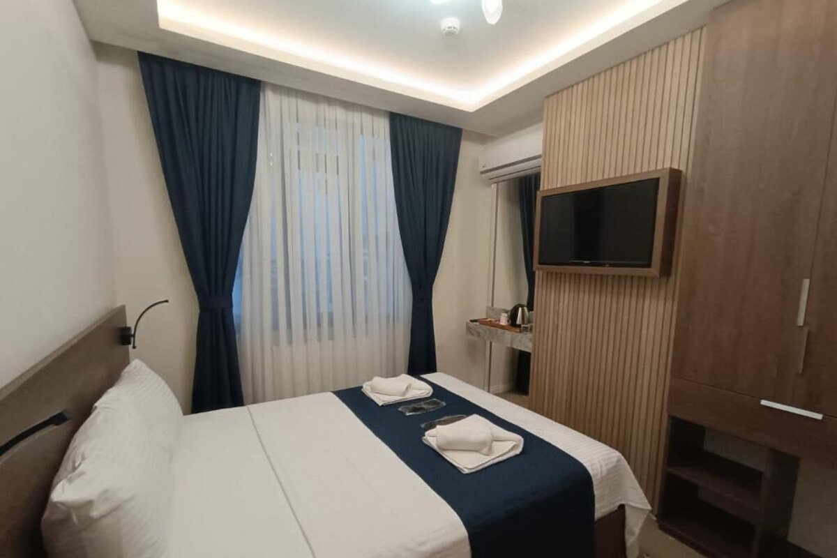 Una habitación de hotel con cama, cortinas, televisor y armario.