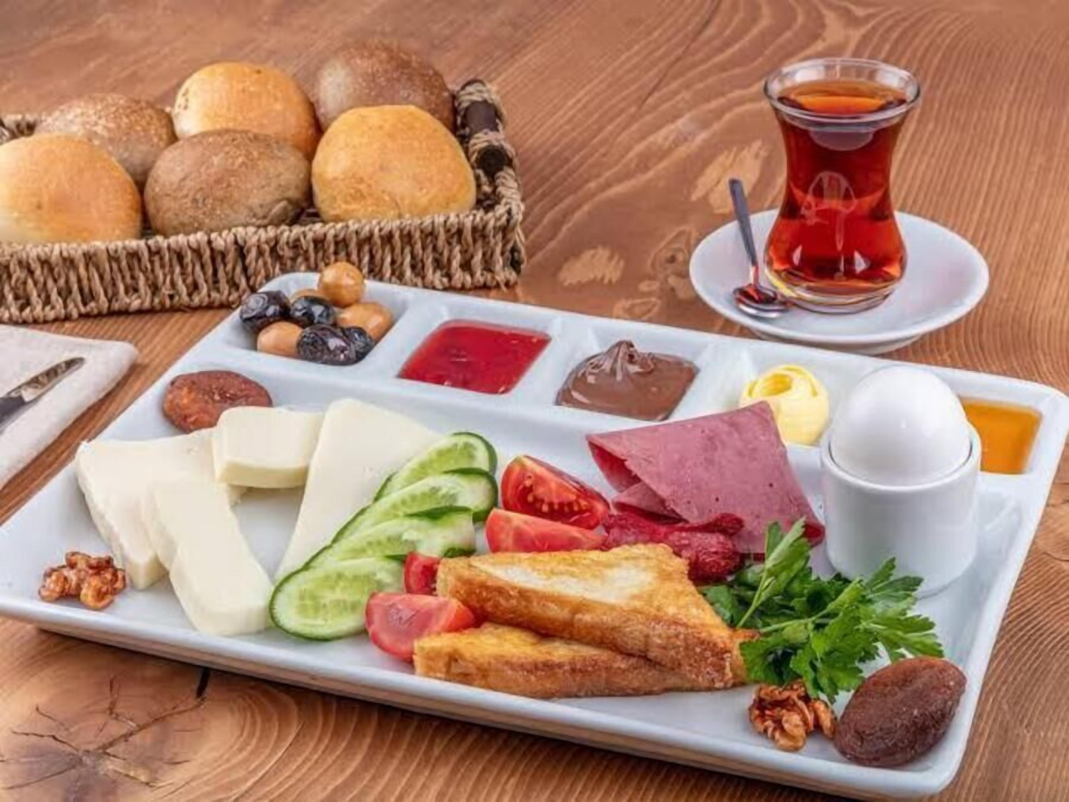 Un assortiment de produits pour le petit-déjeuner, comprenant du pain, du fromage, de la charcuterie et une tasse de thé, disposés sur une table en bois.