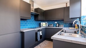 A modern kitchen with dark cabinets, a microwave, a stove, and a sink. - Kneeton Vale (Nottingham)