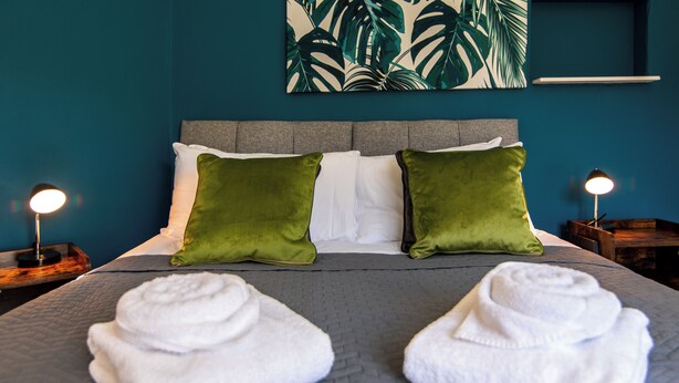 A neatly made bed with two green and two white pillows, a gray quilt, and two rolled white towels on a textured gray bedspread. - Kneeton Vale (Nottingham)