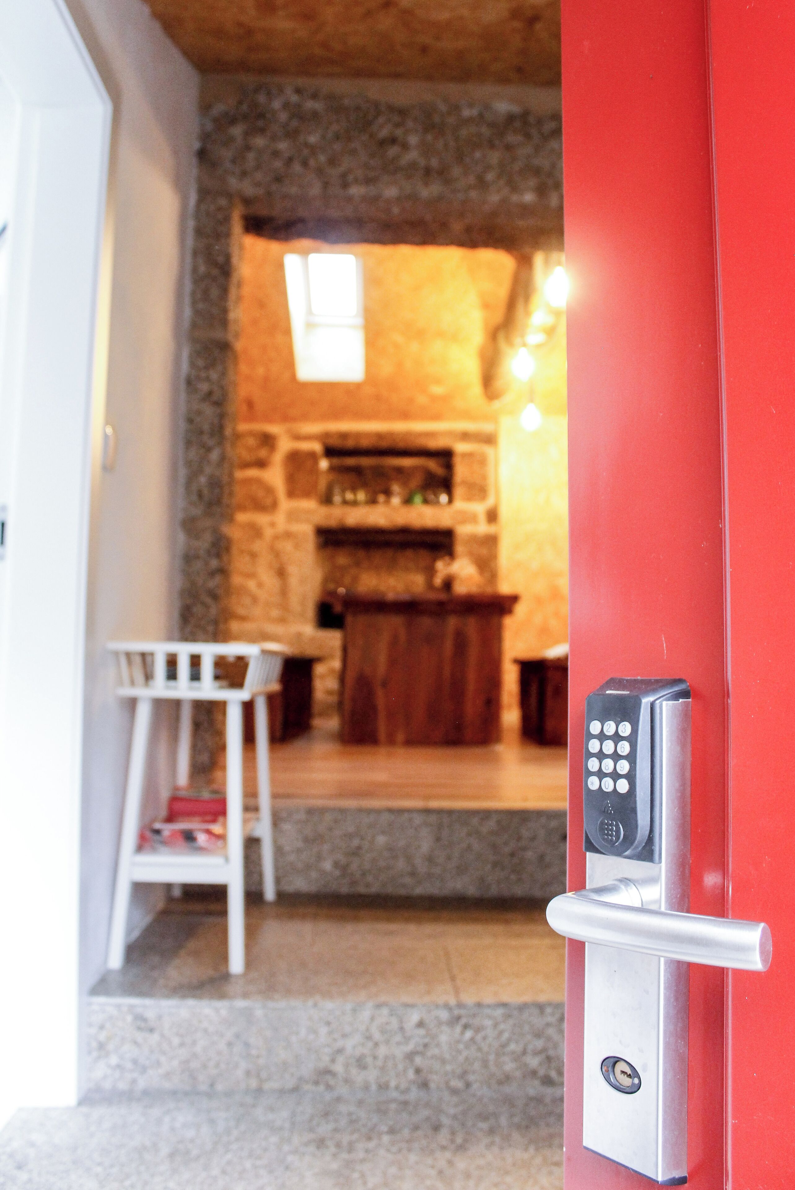 Un vestíbulo moderno con una puerta roja, un candado con teclado numérico y una pequeña silla blanca.