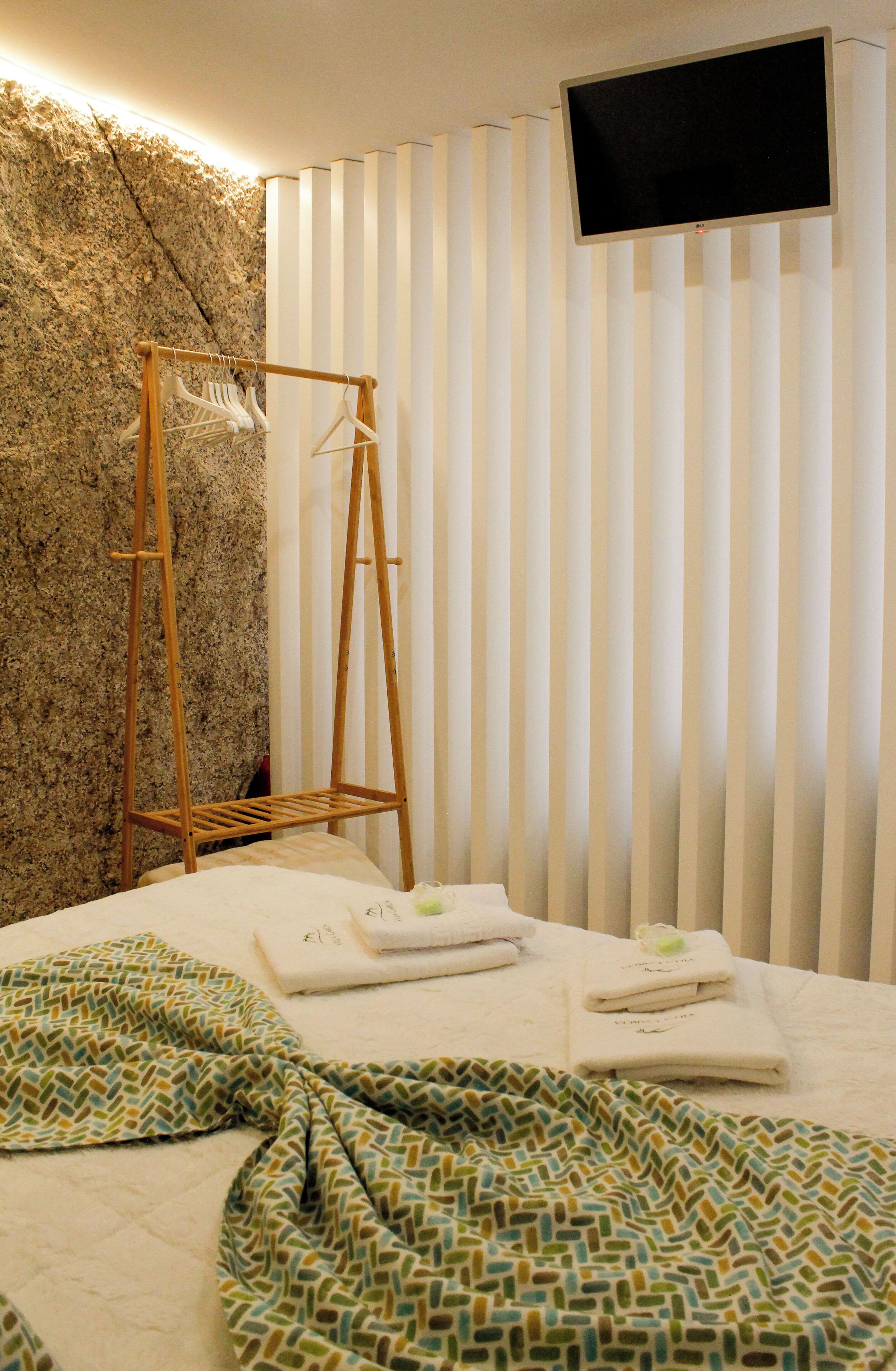 Una habitación de hotel con una cama, un tendedero de madera y un televisor montado en la pared.