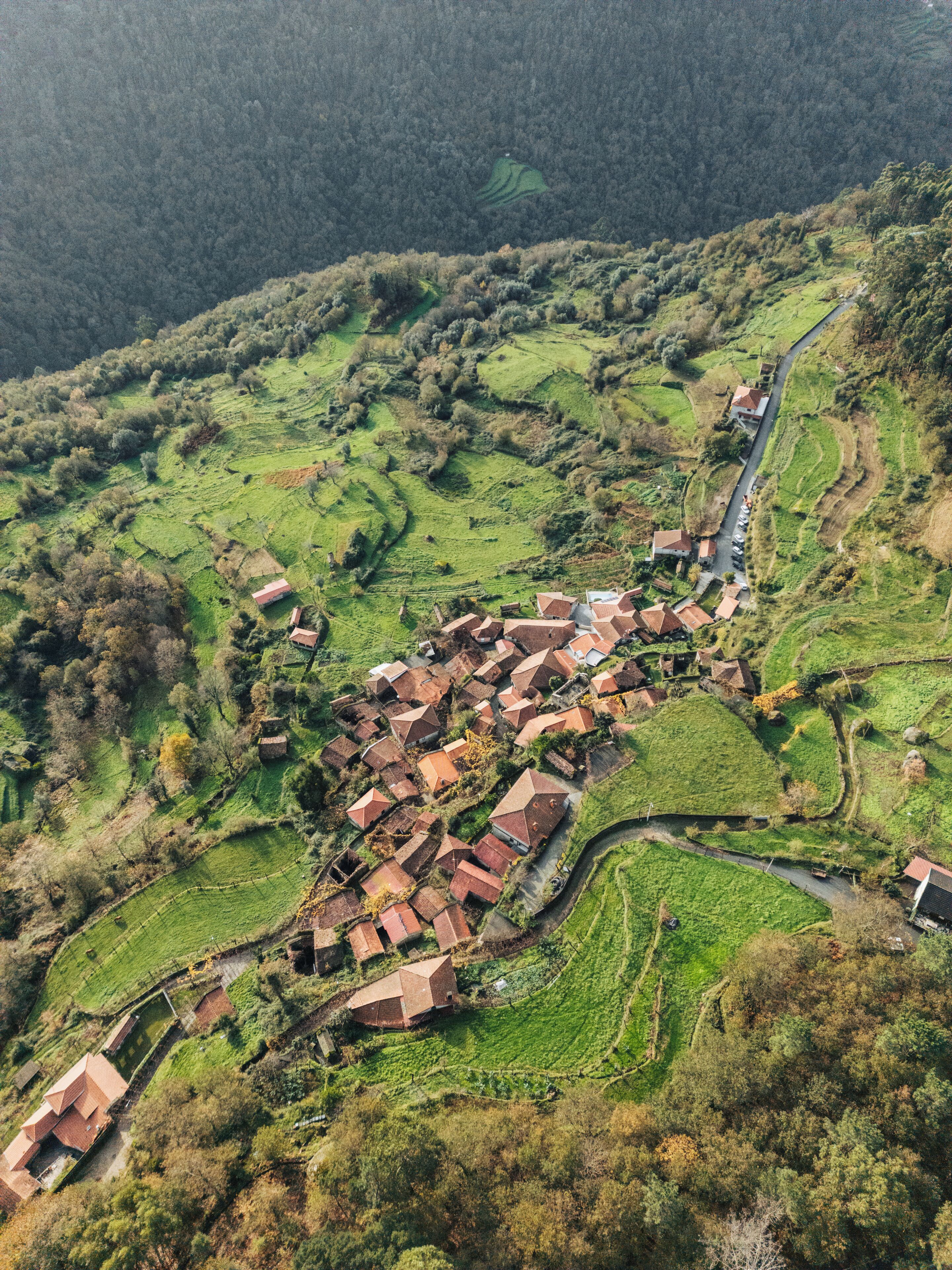 Vue aérienne d’un village avec des champs en terrasses et des maisons aux toits rouges.