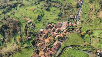 Vista aérea de un pueblo con campos en terrazas y casas con tejados rojos.