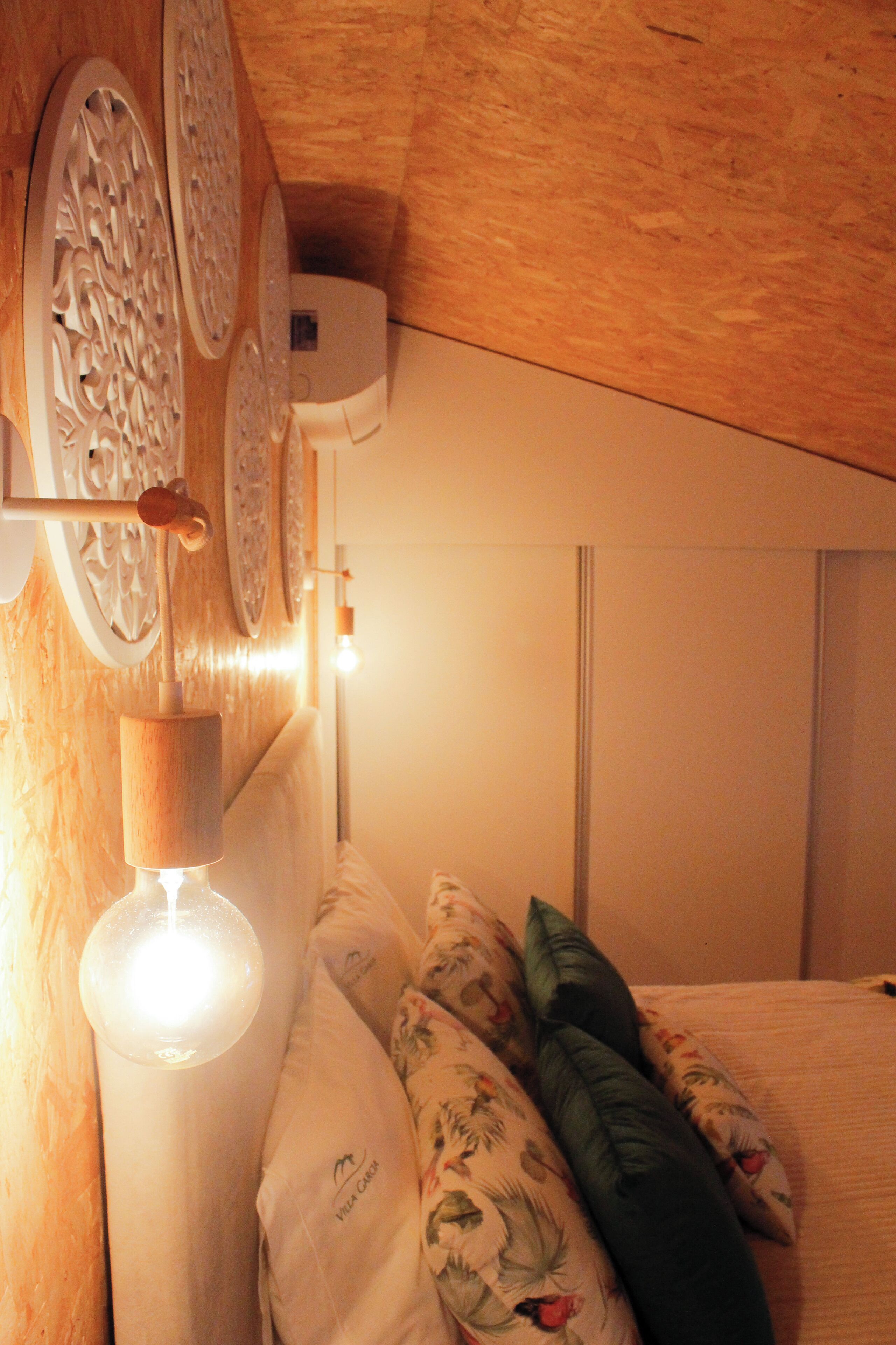 A bedroom with a wooden headboard, a wall-mounted air conditioner, and a bedside lamp.