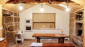 A rustic kitchen with stone walls, wooden beams, a wooden table, and a small cart. - Villa Garcia (Terras de Bouro)