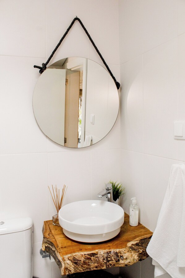 A bathroom with a round mirror, wooden countertop, white sink, and a towel hanging on the wall. - Villa Garcia (Terras de Bouro)