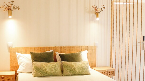 A neatly made bed with a green throw blanket and pillows, wooden headboard, and bedside lamps. - Villa Garcia (Terras de Bouro)