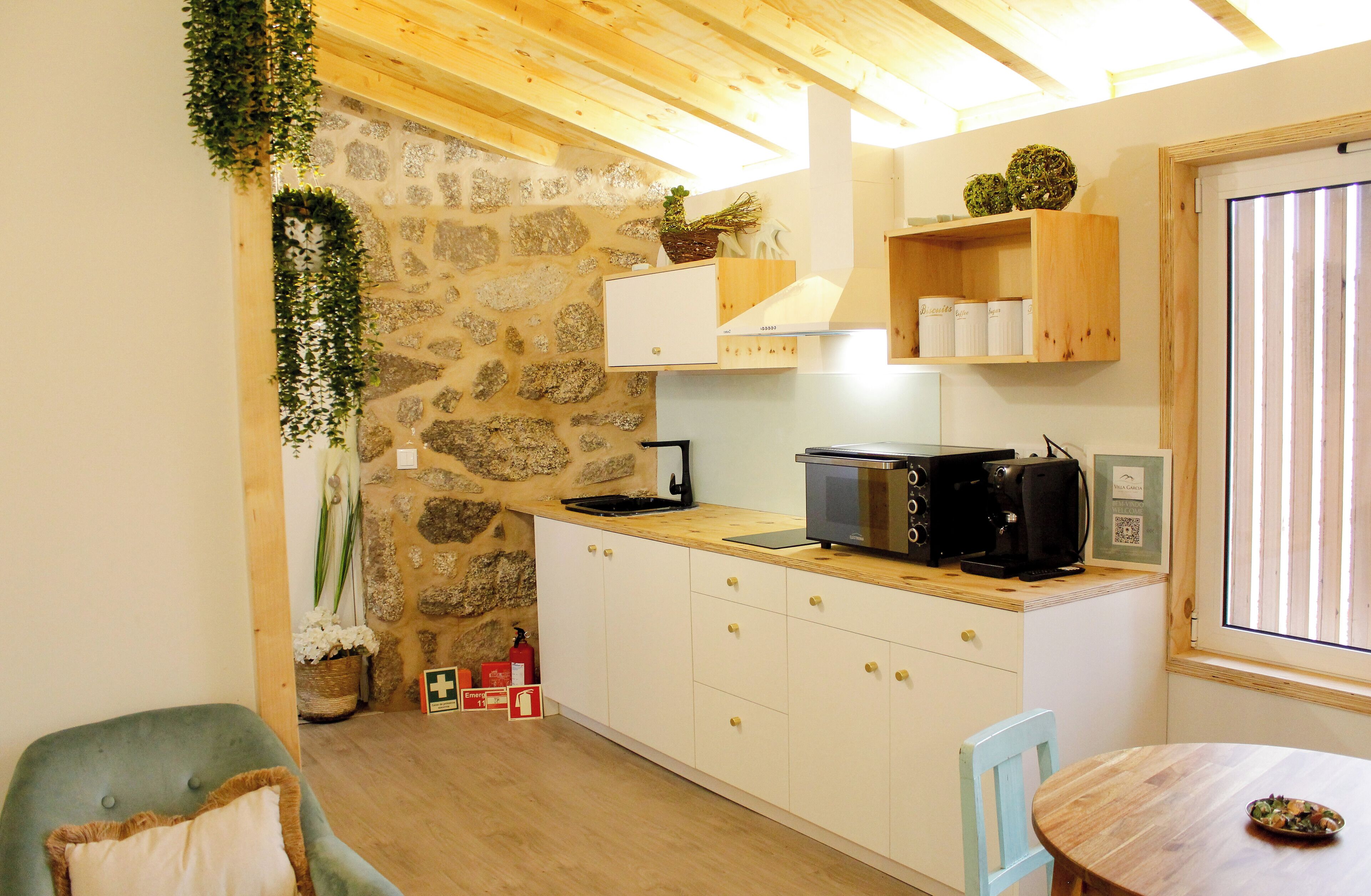 Una cocina compacta con paredes de piedra, armarios de madera, microondas y cafetera.