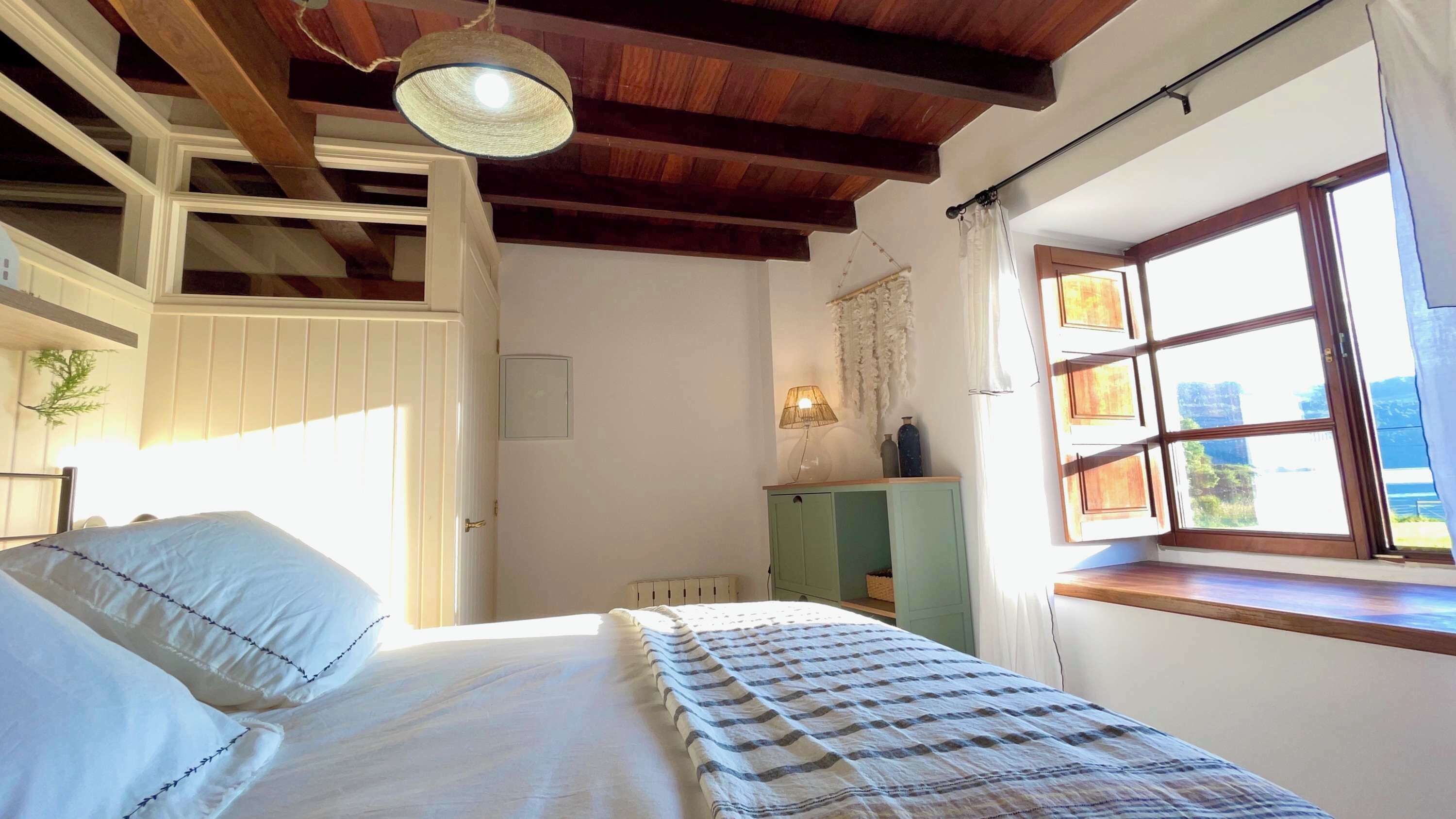 Un dormitorio con cama, ventana con vistas, lámpara colgante y puerta.