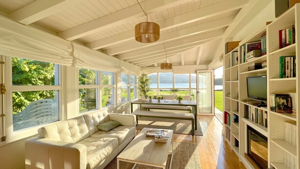 A sunlit room with a white sofa, a coffee table, a TV, and a bookshelf filled with books. - The Cliffs - Cedeira Bay (Cedeira)
