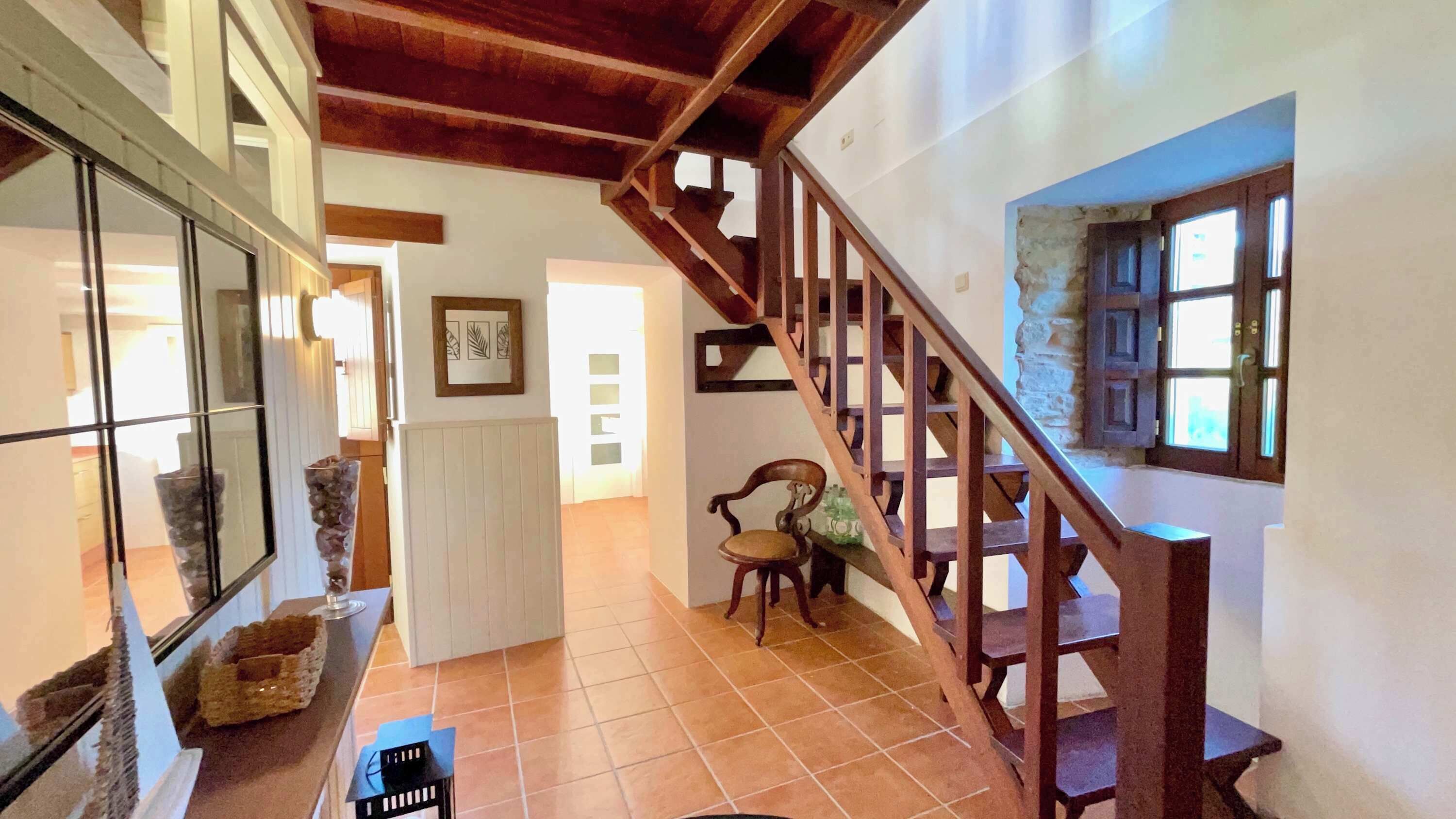 Un hall d’entrée spacieux avec un escalier en bois, une chaise et un radiateur.