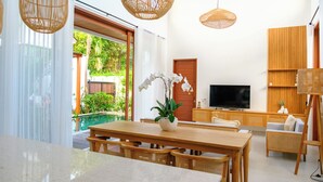 Una sala de estar moderna con una mesa de comedor de madera, sillas de mimbre, un televisor y un amplio ventanal con vistas a un jardín.