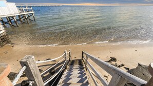 Una scala di legno che conduce a un molo su una spiaggia con acqua cristallina e un orizzonte lontano.