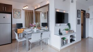 A modern kitchen with a refrigerator, two TVs, a dining table with chairs, and a large mirror. - Herzlia Pituah apartment with Pool, by the Acadia Beach! (Herzliya)