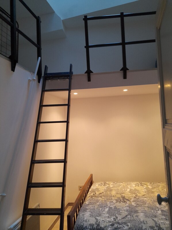 A bunk bed with a wooden ladder, a patterned bedspread, and a small window.