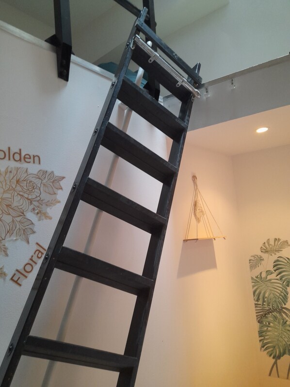 A black metal ladder leaning against a wall with floral wall art and the words "Golden Floral" visible.