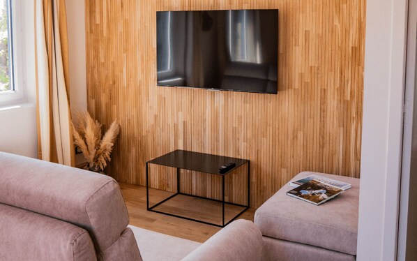 Una sala de estar moderna con un televisor de pantalla plana montado en una pared de madera, una mesita auxiliar negra y dos sofás rosados.
