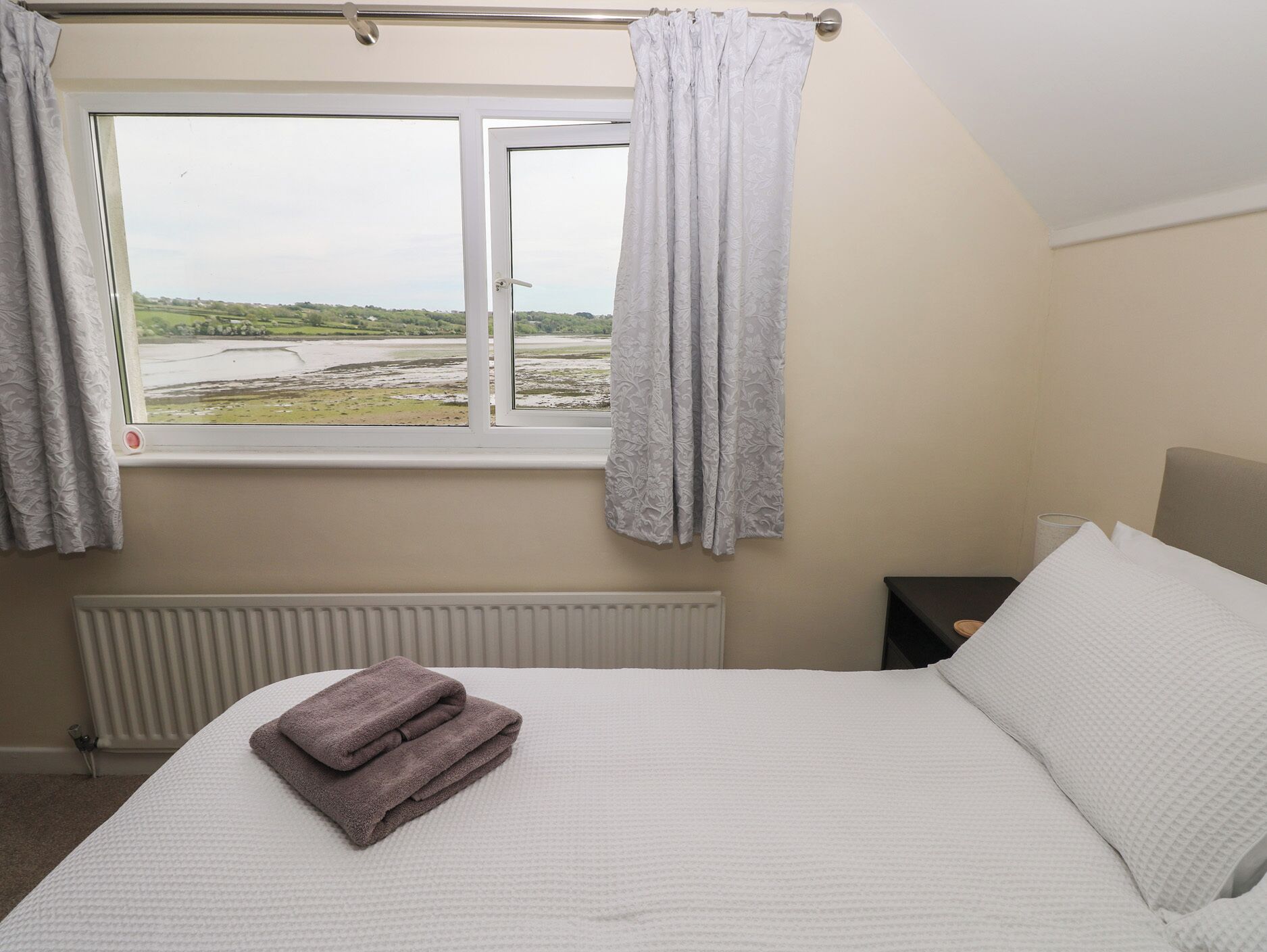 Un dormitorio con cama, ventana con cortinas, radiador y vistas al paisaje.