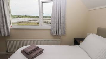 Un dormitorio con cama, ventana con cortinas, radiador y vistas al paisaje.
