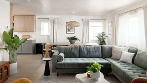 A modern living room with a green sofa, a coffee table, and a dining area with a table and chairs. - Pool & Palmz|Hot Tub|Fire Pit|Chefs Kitchen|6 beds (San Diego)
