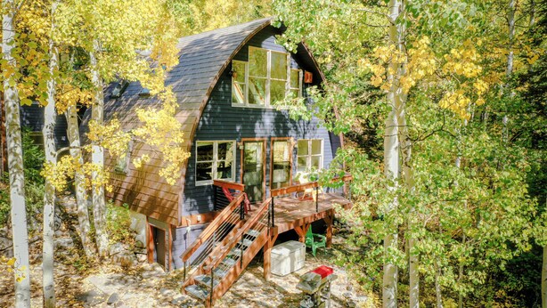 Una cabaña con terraza de madera, una escalera y un ventanal grande con vistas a un bosque.