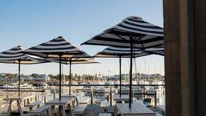 Buiten zitplaatsen met gestreepte parasols met uitzicht op een jachthaven met boten.