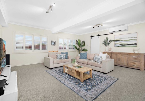 A spacious living room with two sofas, a coffee table, and a large window with blinds.