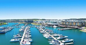 A marina with numerous boats docked, a modern building, and a waterfront promenade.