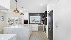 Een moderne keuken met witte kasten, een marmeren eiland, roestvrijstalen apparatuur en hanglampen.
