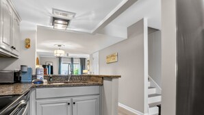 Cocina con encimeras de granito, armarios blancos, extractor de acero inoxidable y vistas al comedor.