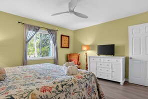 A bedroom with a bed, a dresser, a chair, a television, and a window with curtains.