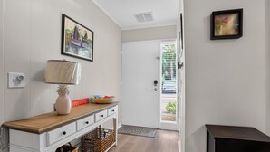 Un pasillo con una puerta blanca, un cuadro enmarco, una lámpara, una cesta y un letrero.