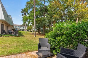 A patio with wicker furniture, a grassy lawn, and a building in the background.