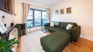 A modern living room with a green sofa, a small table, a potted plant, and a large window with curtains. - Stylish and trendy 2bed apartment in city centre. (Dublin)