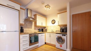 A compact kitchen with white cabinets, a built-in oven, a microwave, a dishwasher, and a washing machine. - Stylish and trendy 2bed apartment in city centre. (Dublin)