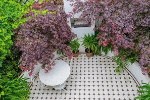 A tiled patio with a round table and chairs, surrounded by potted plants and trees.